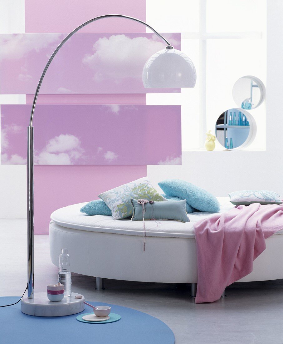 Round bed, standard lamps with marble base and pink photo mural of clouds on wall