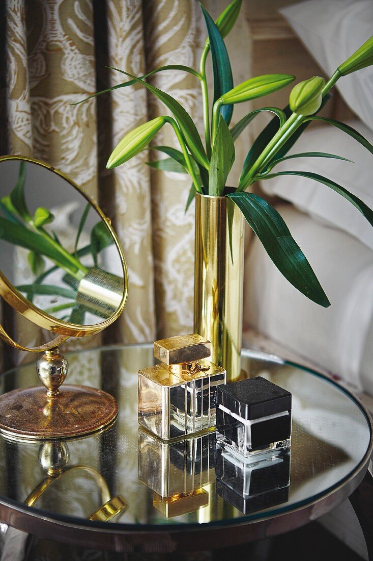 Schminkspiegel, Lilienknospen in Goldvase und Parfum auf verspiegeltem, rundem Nachttisch