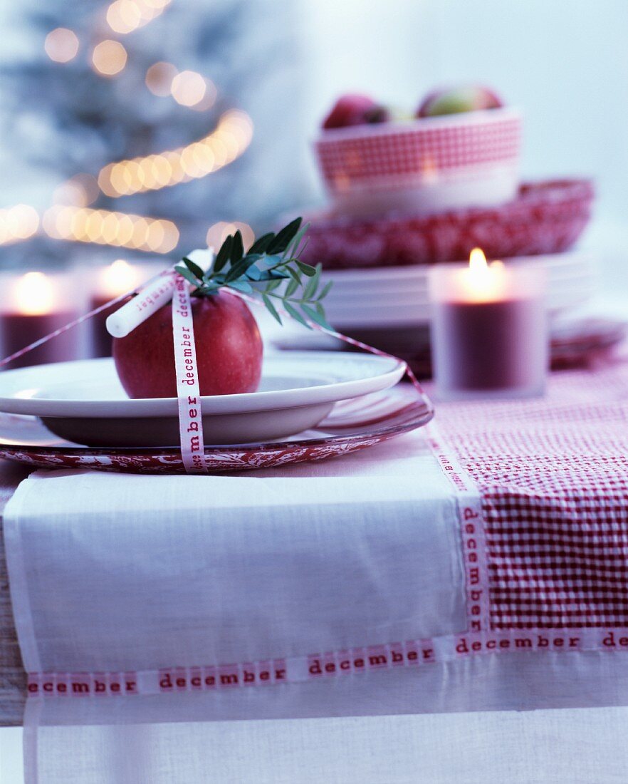 Tischgedeck weihnachtlich dekoriert mit rotem Apfel, Kerze und Dekoband