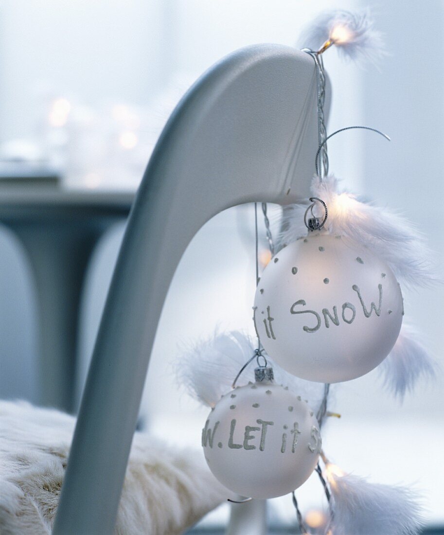 Chair with fur seat cover decorated with string of fairy lights and feathers and white baubles with festive mottoes