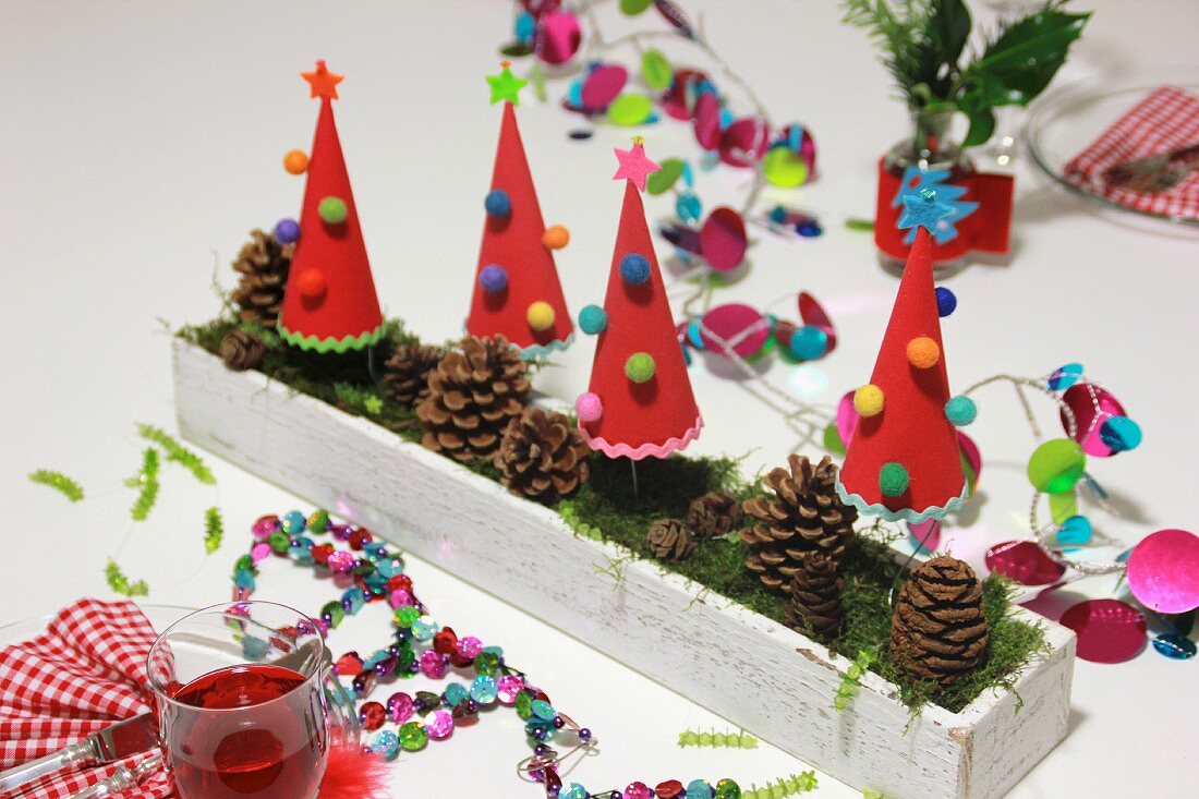 Hand-crafted, festive table decoration with garlands, paper Christmas trees & pine cones