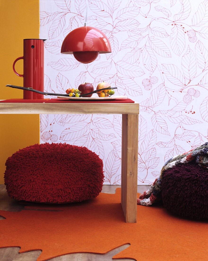 Herbstliche Zimmerdeko mit orangenem blattförmigen Teppich, roten Sitzpoufs und Wandtapete mit Blättermotiv