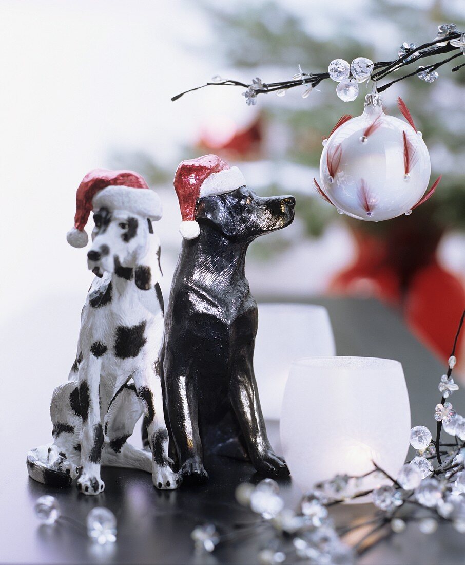 Christmas arrangement of two black and white dog ornaments wearing Father Christmas hats next to twigs decorated with glass beads