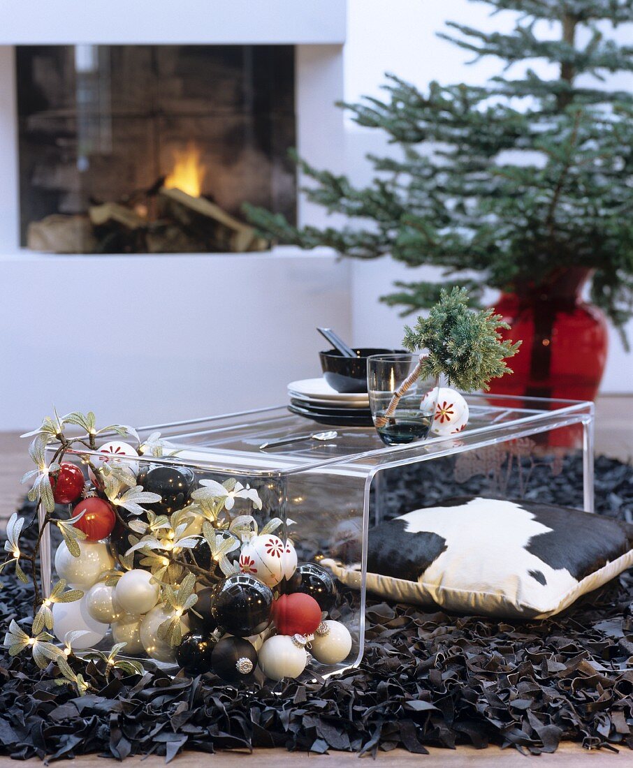 Plexiglas coffee table on black designer rug made from strips of leather in festively decorated interior with fireplace