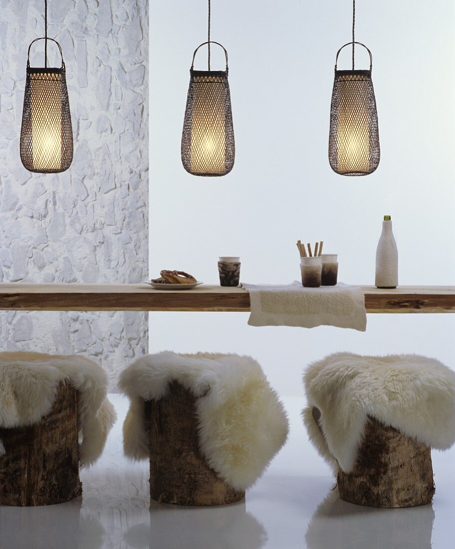 Sheepskin rugs on tree stump stools at rustic wooden table below decorative bamboo pendant lamps
