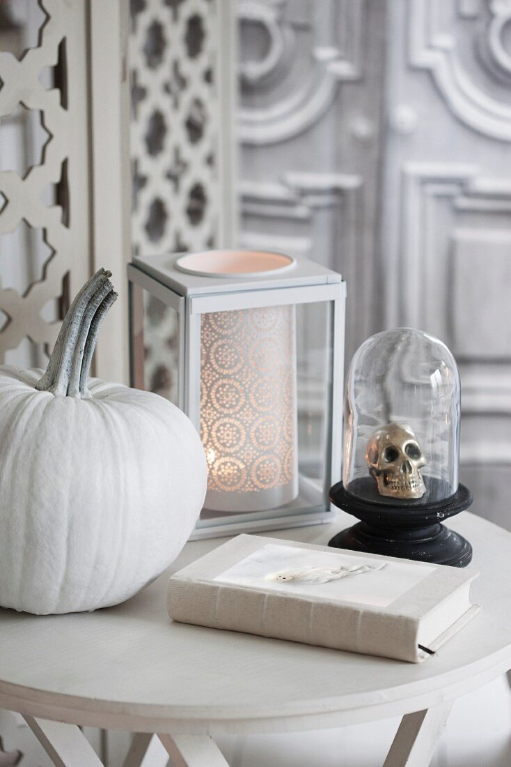 Halloweendeko auf Tisch, weiss lasierter Kürbis, Deko Totenschädel unter Glashaube und romantisches Windlicht
