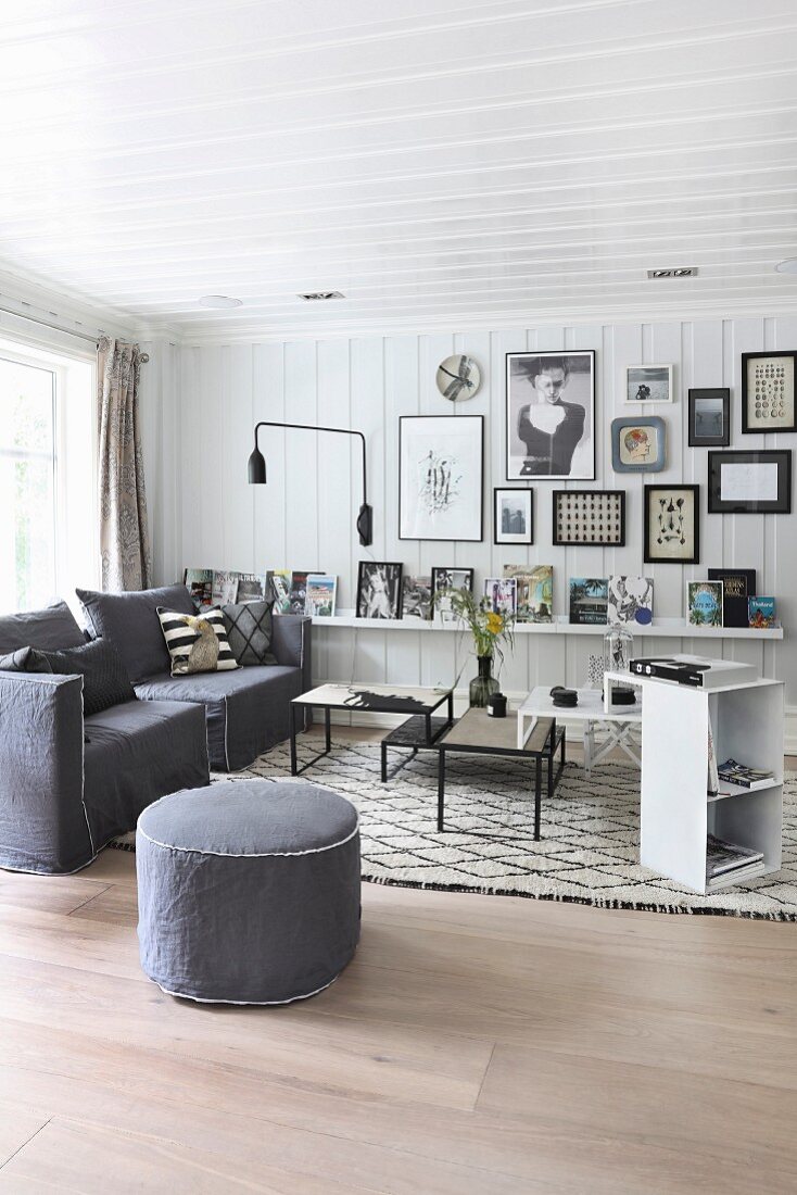 Skandinavischer Wohnraum mit weisser Holzverschalung, graue Sessel und Sitzpouf vor mehrteiligem Couchtisch-Set