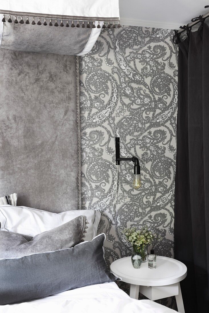 Bed and white side table against wall covered in ornate wallpaper