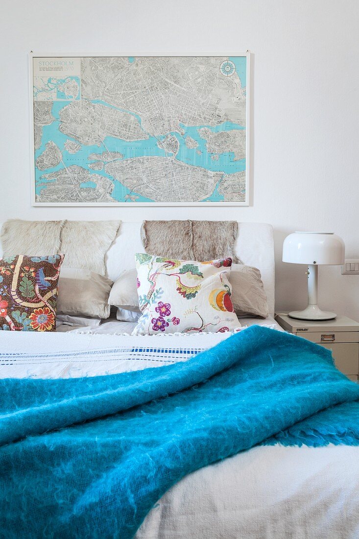 Doppelbett mit blauer Tagesdecke, Landkarte an Wand, seitlich Retro Tischleuchte auf Nachttisch