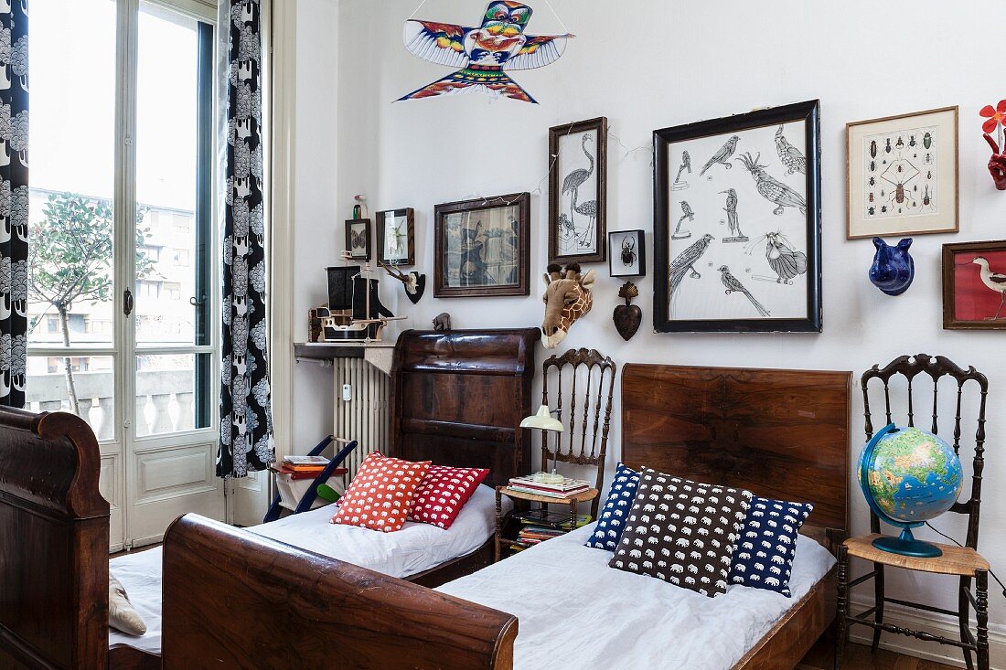 Zwei antike Schlittenbetten aus dunklem Holz und gemusterte Kissen, dazwischen Stühle als Nachttisch, oberhalb gerahmte Bilder mit Vogelmotiven an Wand