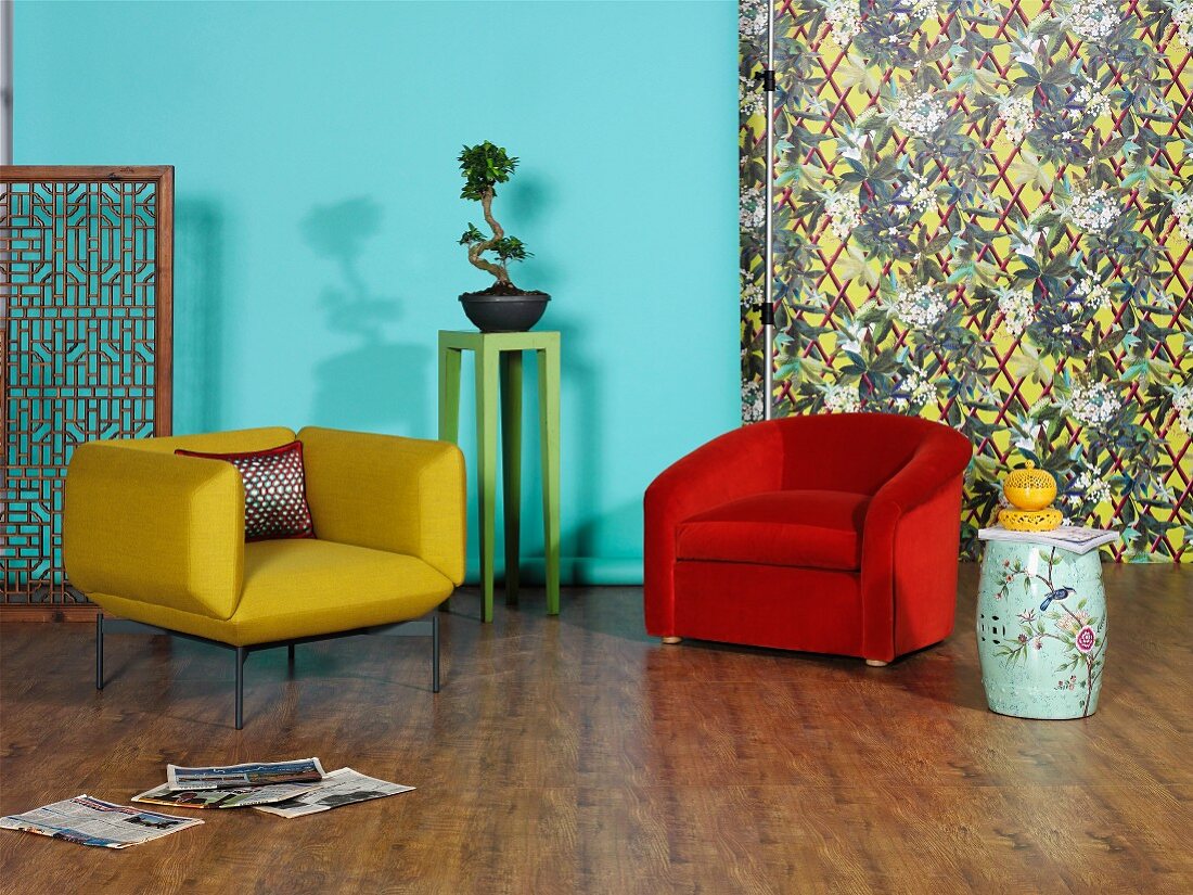 Retro armchairs in yellow and red, Chinese porcelain accessories and Bonsai tree against turquoise wall and patterned wallpaper