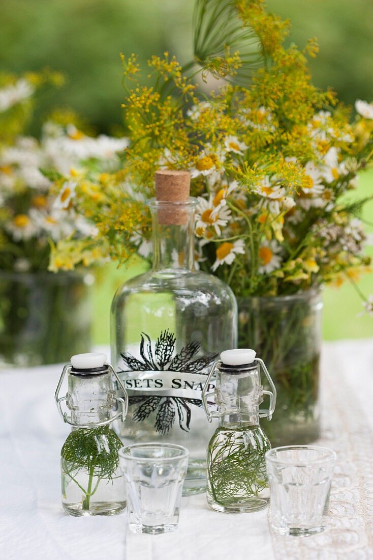 Herbs in swing-top bottles, large corked bottle and vase of flowers on garden table