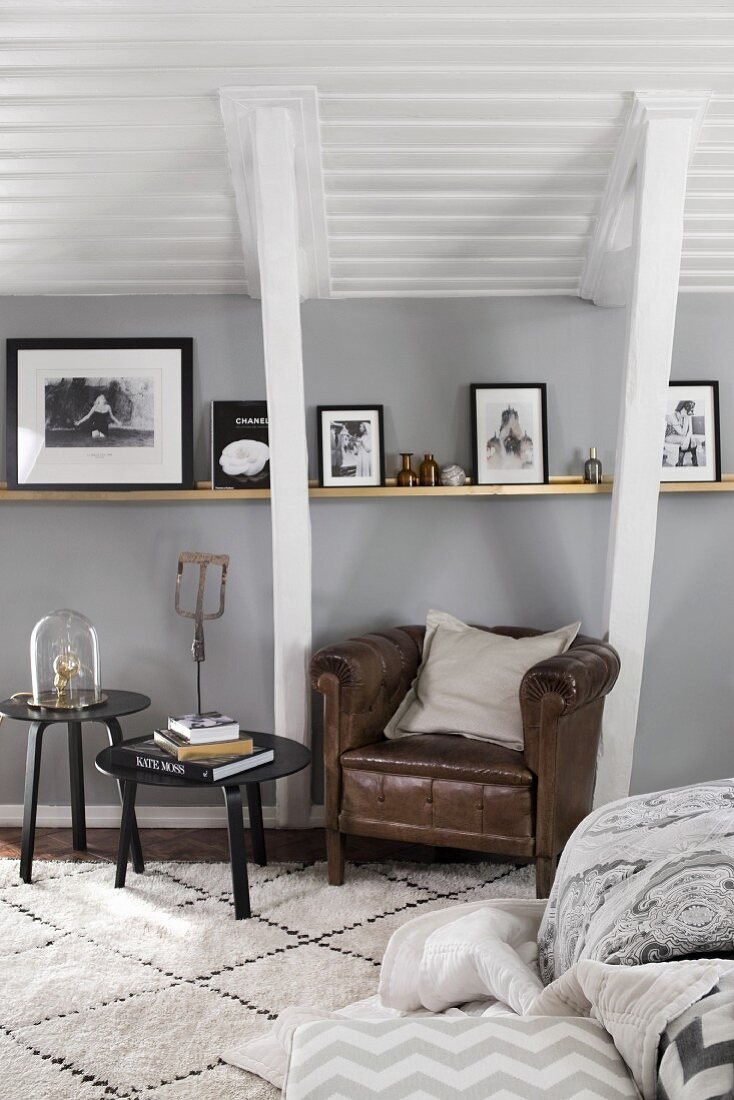 Leather armchair and side table below pictures on narrow shelf and sloping ceiling