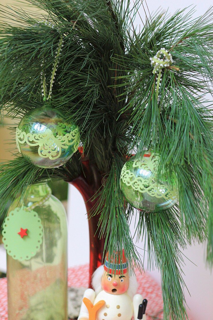 Glass baubles decorated with green trim hung from pine branch