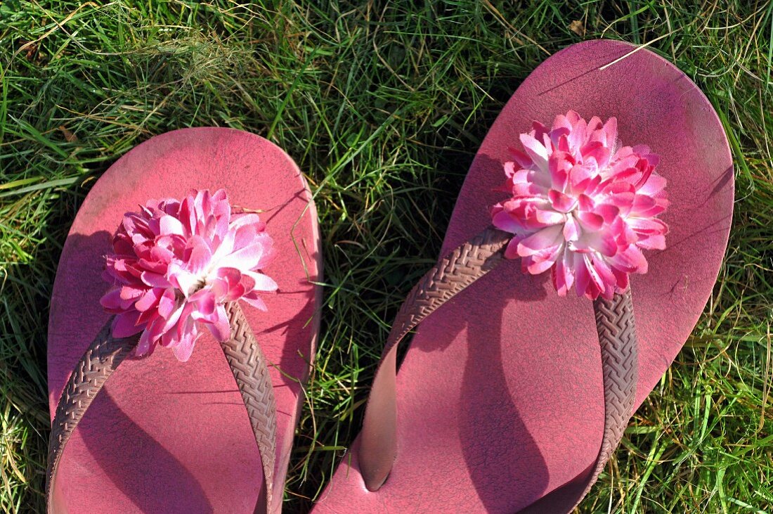 Pink flip-flops with artificial flowers on straps on lawn