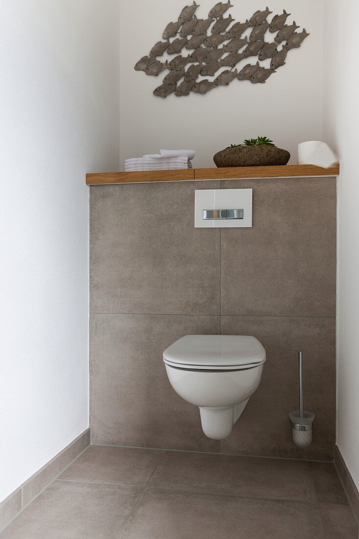 A fish wall decoration above a grey-tiled fronting wall with a toilet
