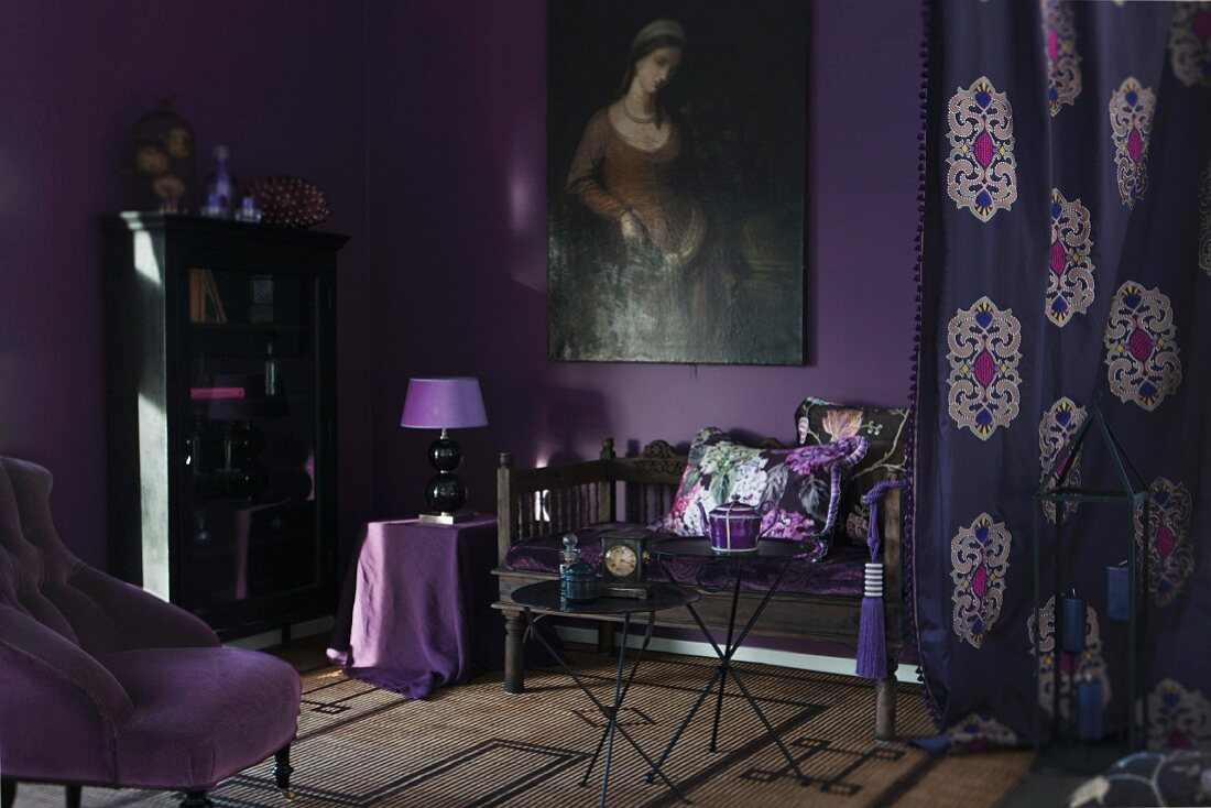 Zimmer in Violettfarben, Sessel mit mauve Bezug und antike Sitzbank an auberginefarbener Wand mit Ölgemälde, seitlich gemusterter Vorhang