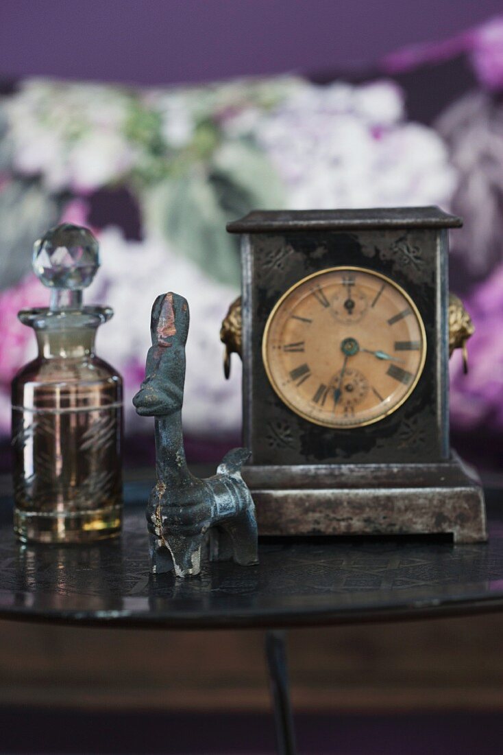 Table clock and ethnic animal figurine next to glass perfume bottle
