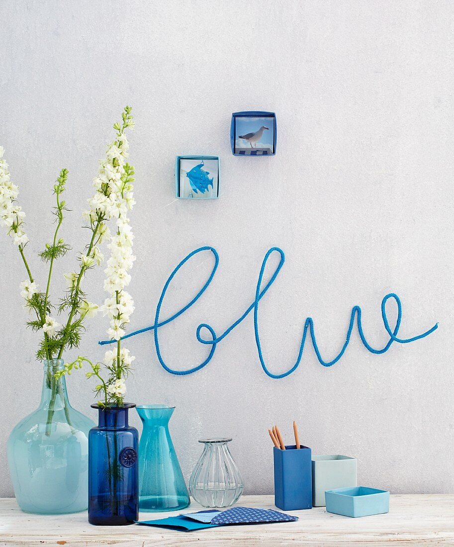 Various blue vases against a wall with the word 'blue' knitted on the wall