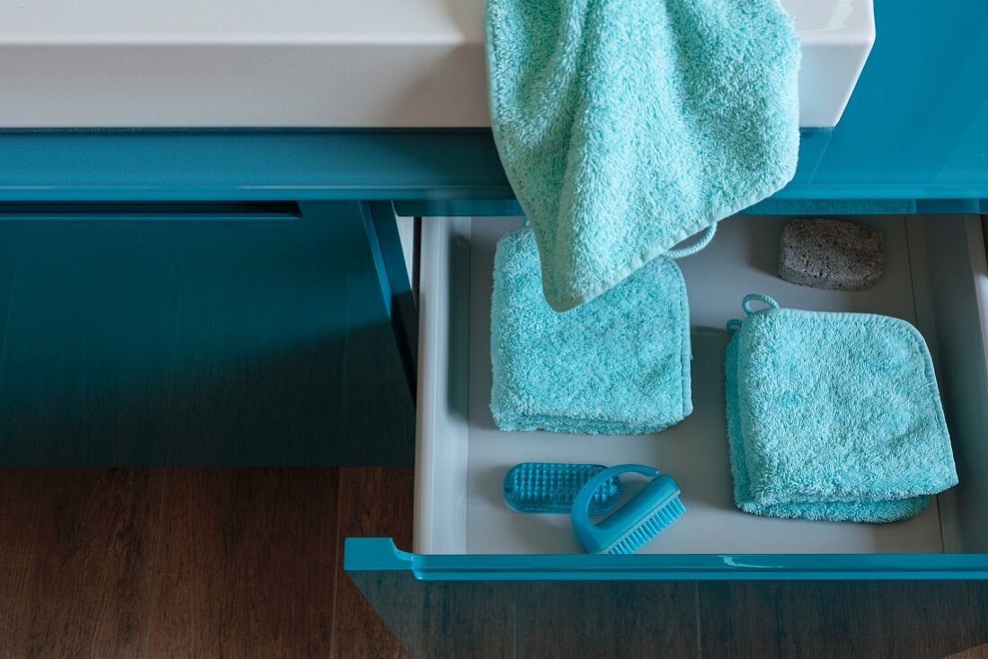 Folded, turquoise towels and washing utensils in an open drawer in a washstand