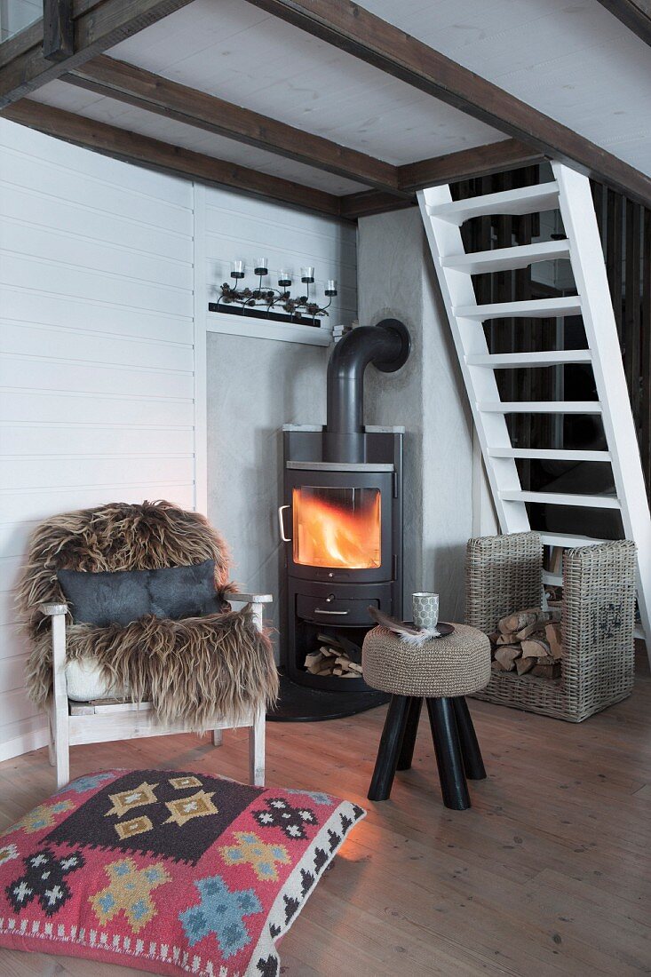 Fur rug on armchair, ethnic floor cushions and stool in front of fire in log burner in cabin