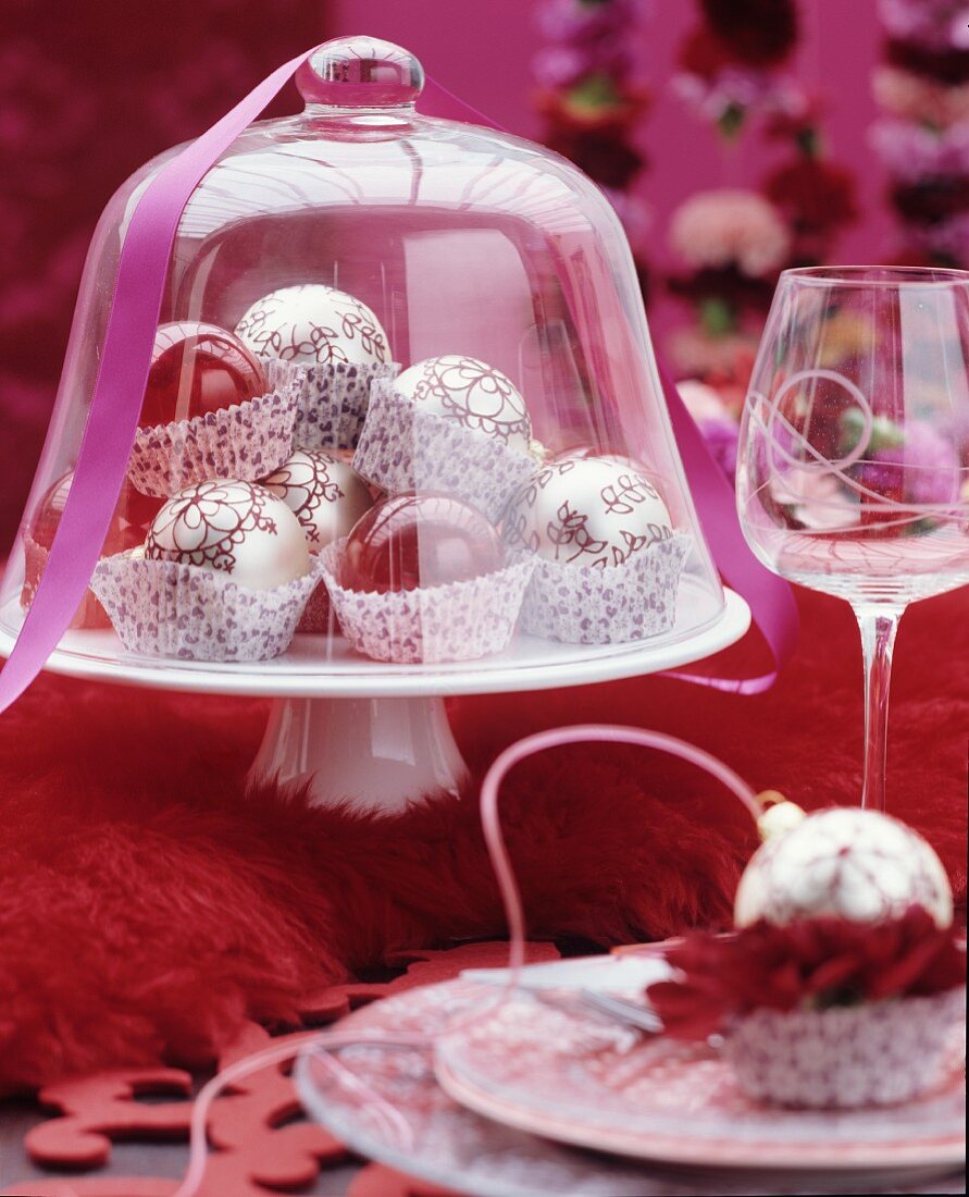 Festive table arrangement of Christmas tree baubles in paper cake cases under glass cover