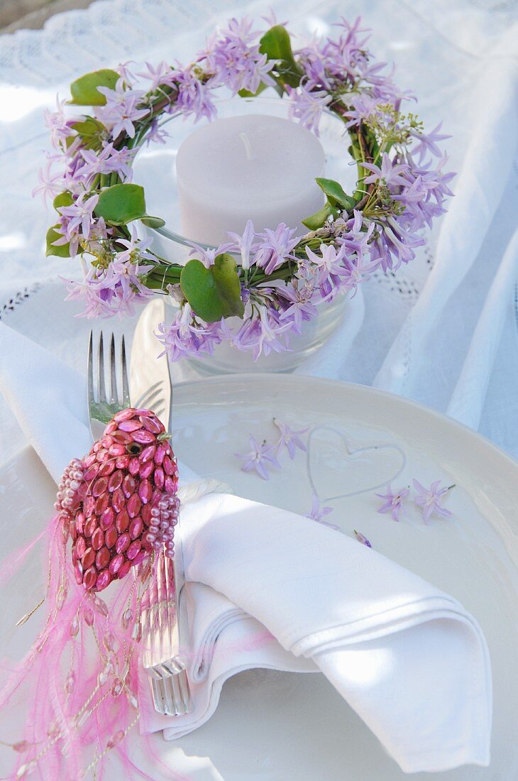 Windlicht dekoriert mit Blumenkranz, mit violetten Blüten und Dekovogel aus pink glitzernden Perlen auf Gedeck