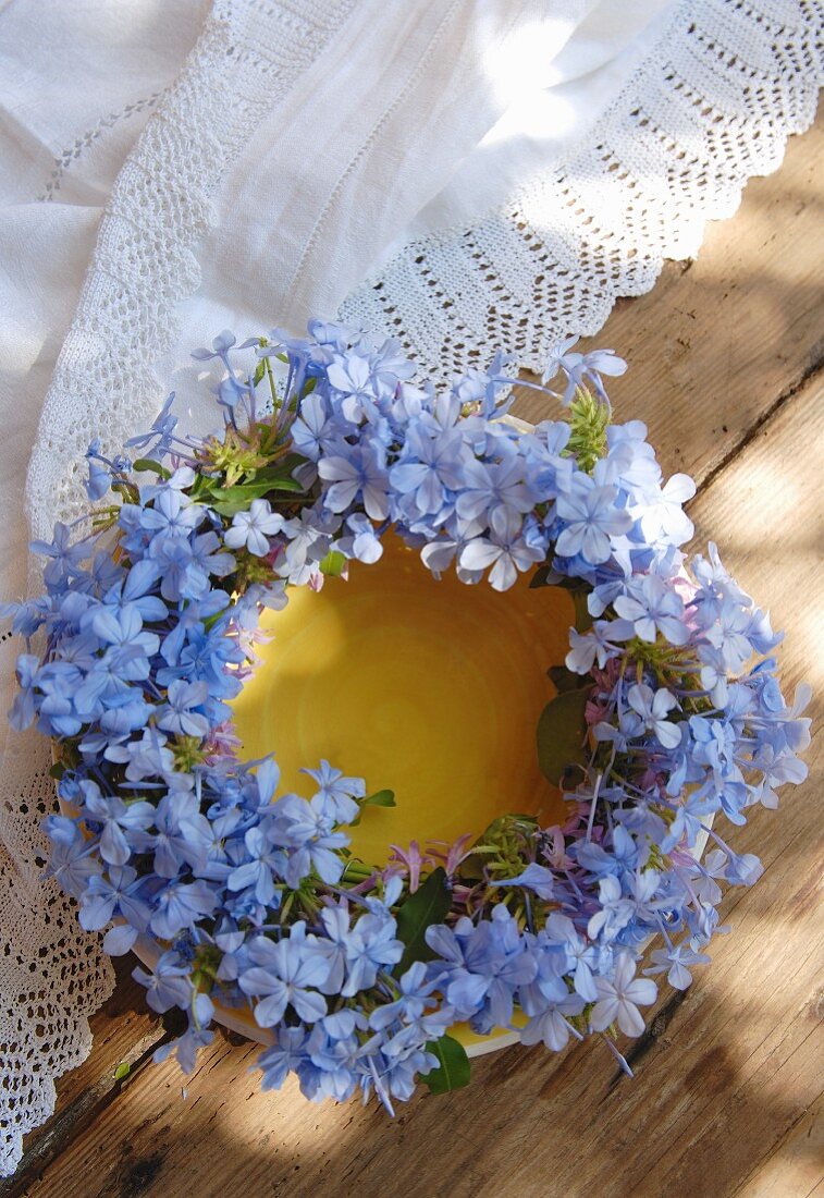 Wreath of purple flowers on yellow plate next to white, lace tablecloth