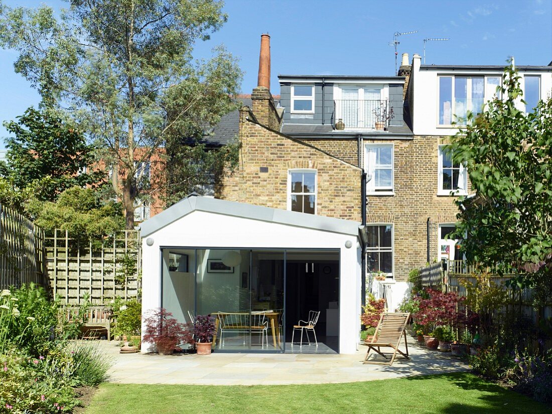 Modern extension on brick façade with glass wall, terrace and lawn