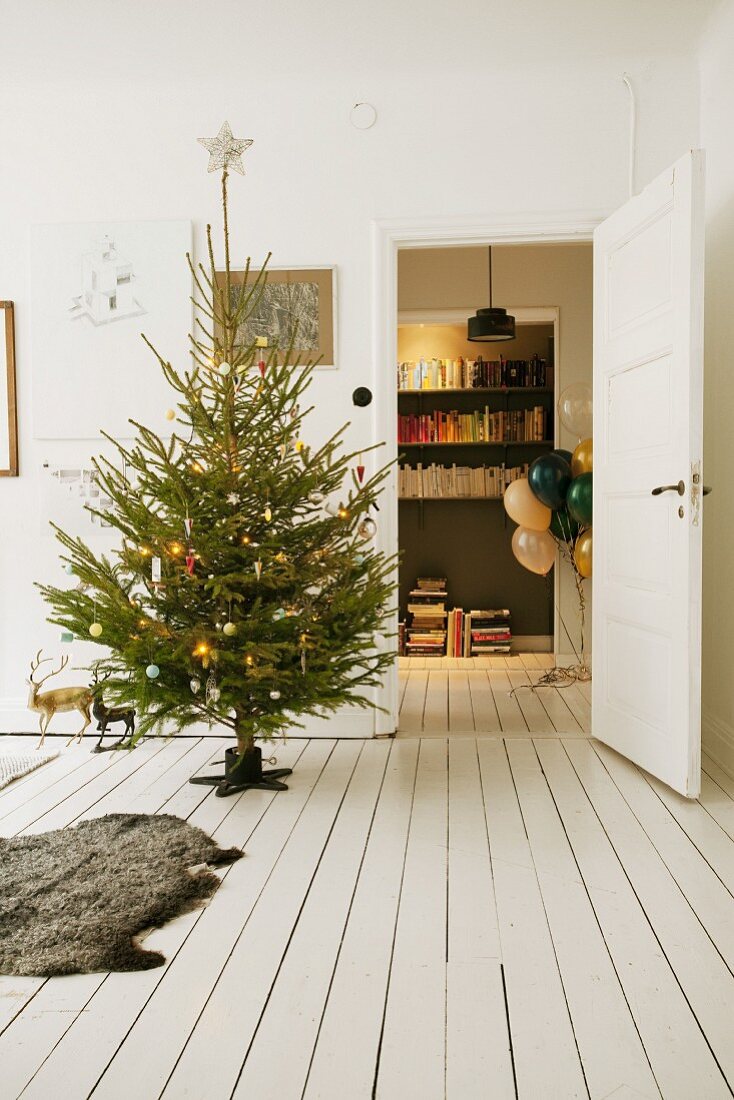 Decorated Christmas tree, animal-skin on white wooden floor and view of balloons and bookcase through open door