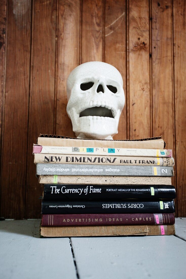 Deko-Totenkopf auf einem Stapel Bücher vor einer Bretterwand