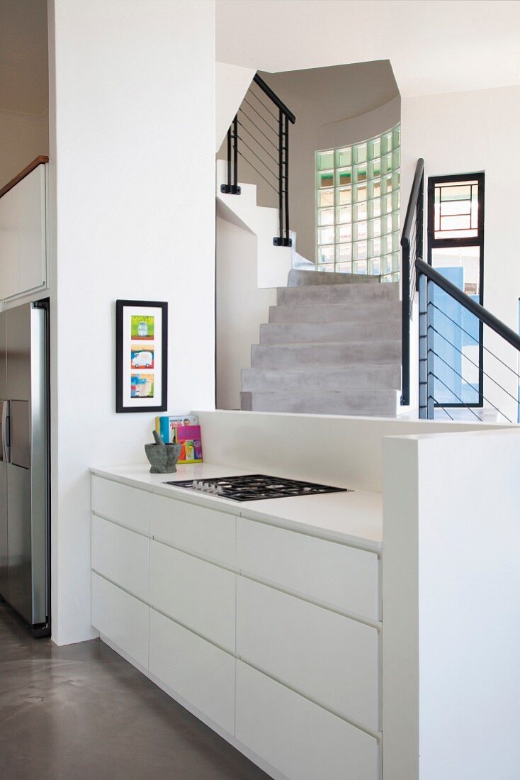 Küchenzeile mit weißem Unterschrank vor Brüstungsmauer, im Hintergrund Treppenaufgang, schwarzes Geländer an Betontreppe
