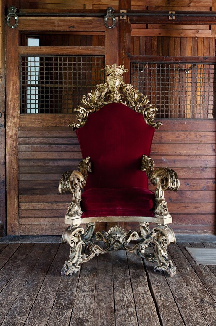 Opulent, ornate gilt throne with red velvet upholstery against board wall