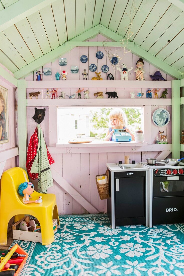 Holz-Spielhaus in Pastellfarben gestrichen und mit Spielzeugfiguren dekoriert, Mädchen am Fenster