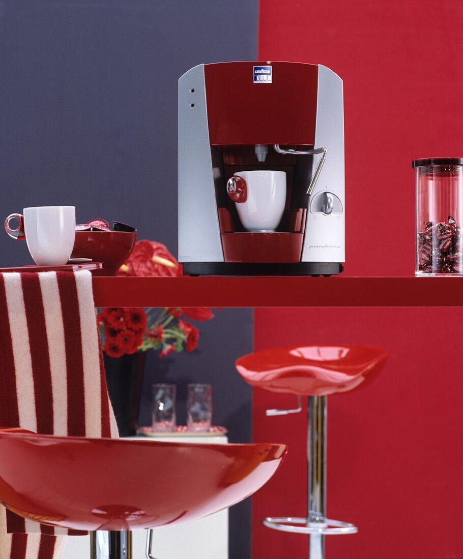 Knallrote glänzende Barhocker an roter Küchentheke mit Espressomaschine und weißen Tassen