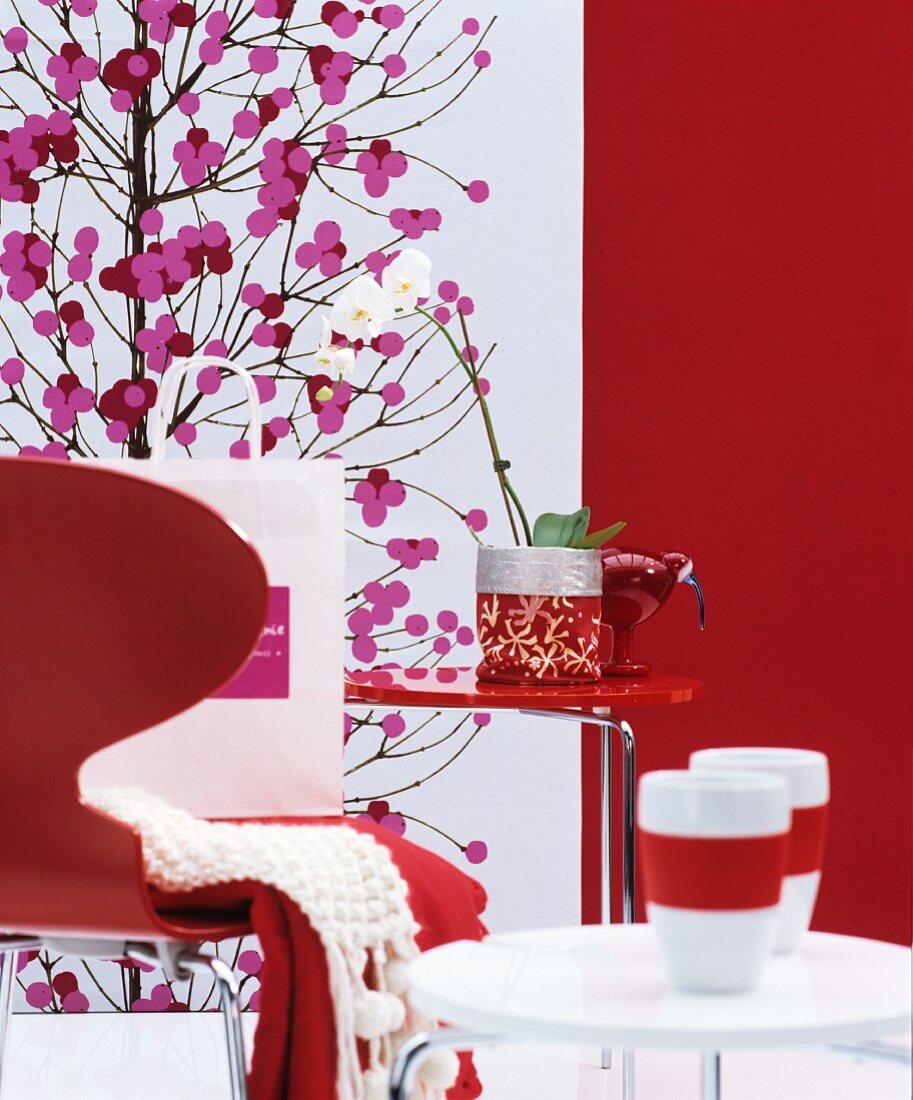 Roter Stuhl mit rotem und weißem Beistelltischen, weiße Orchidee vor roter Wand und Dekoration mit japanischem Blütenmotiv