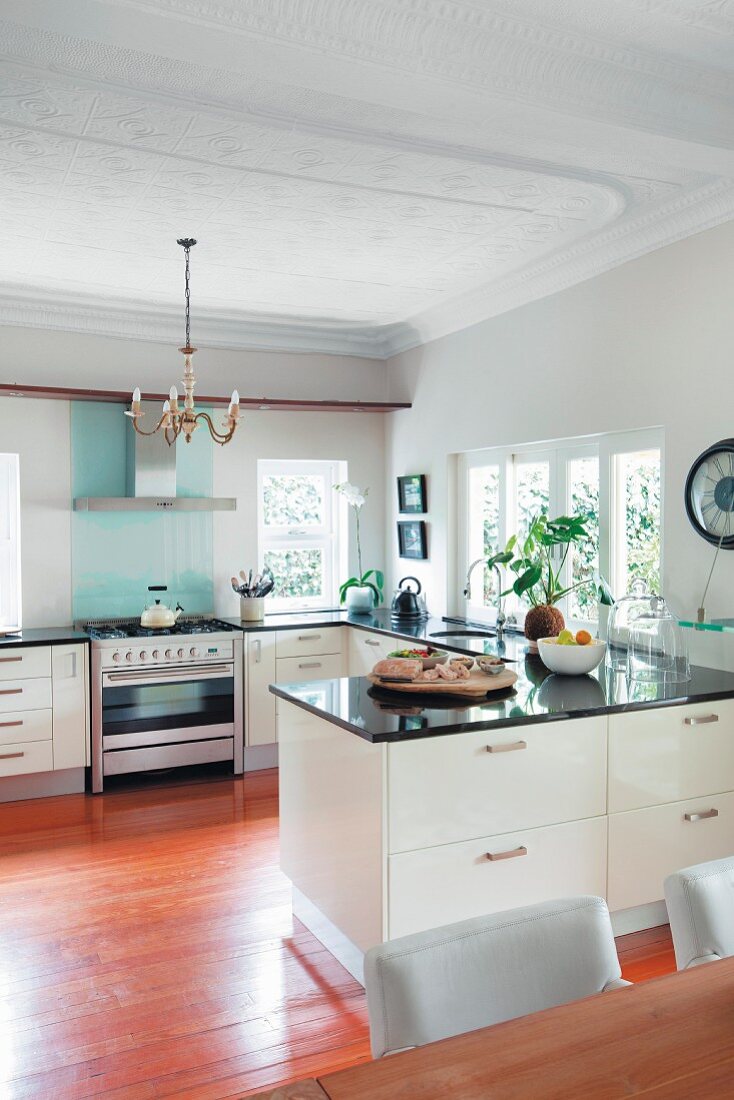 Modern, open-plan, white kitchen with black stone worksurfaces on U-shaped counters and stucco ceiling