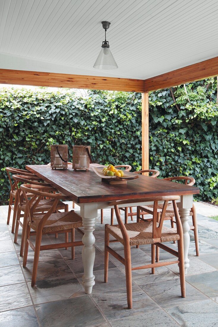 Classic chairs around rustic dining table on roofed terrace