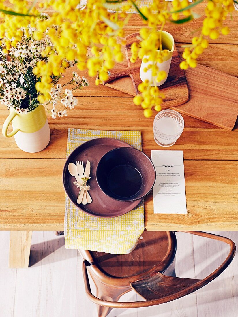 Blick auf gedeckten Tisch mit Holzbrettchen, Menükarte und gelben Blumen