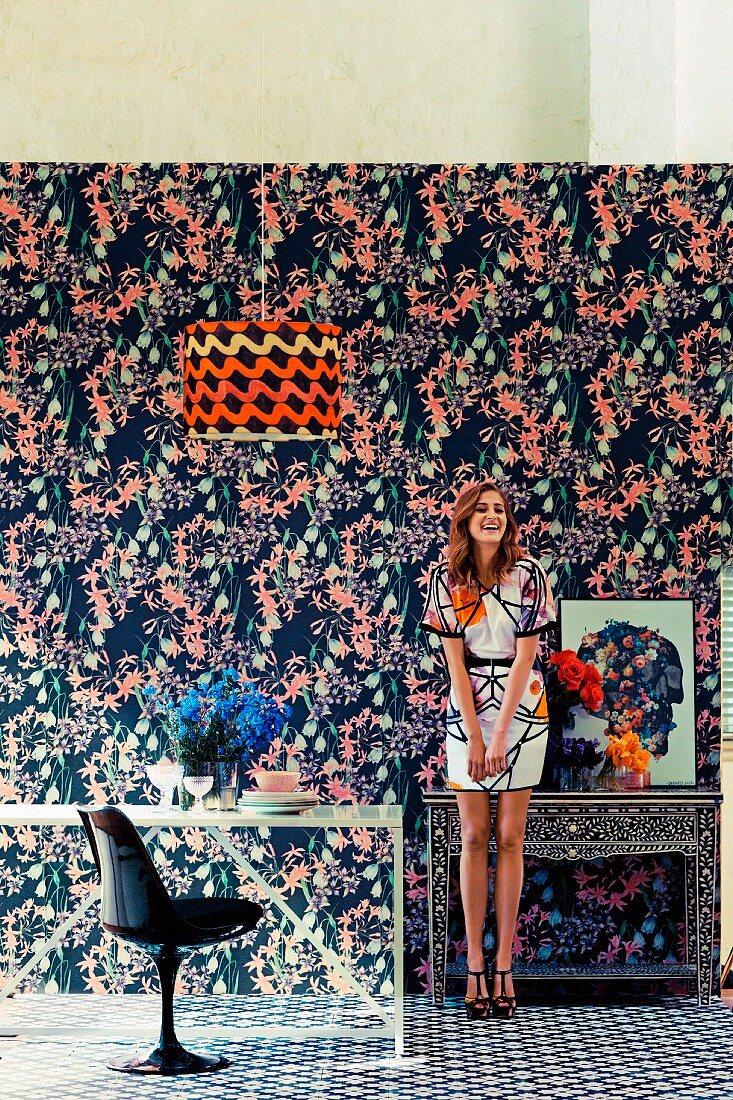 Young woman in room with different patterns on wallpaper, carpet, lampshade and dress