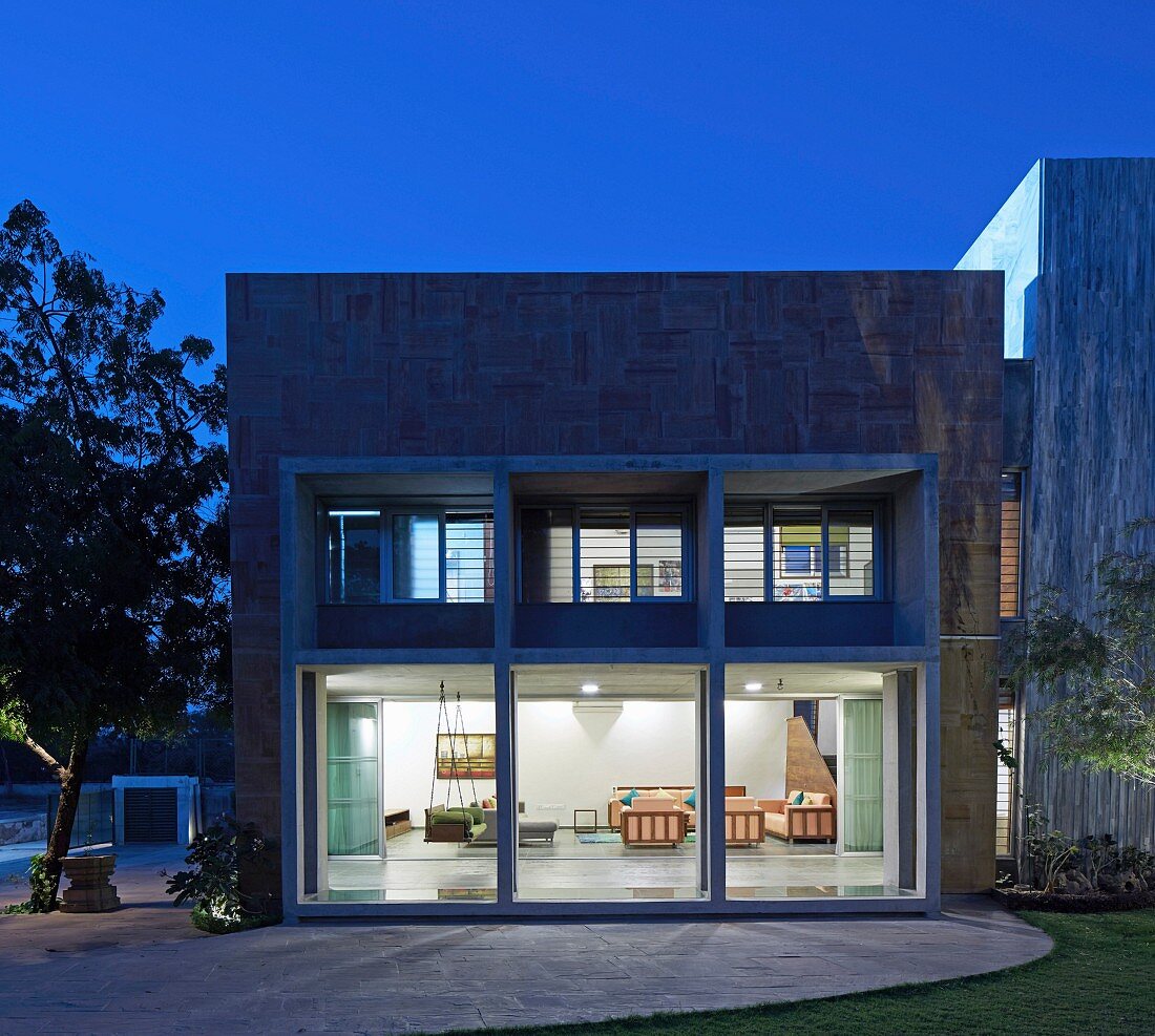 View from garden to contemporary house with illuminated interior at twilight
