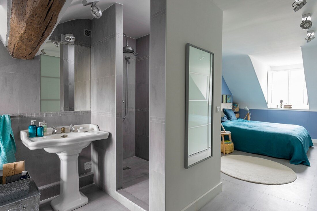 Grey shower area in ensuite bathroom with view into blue bedroom in renovated attic with dormer window