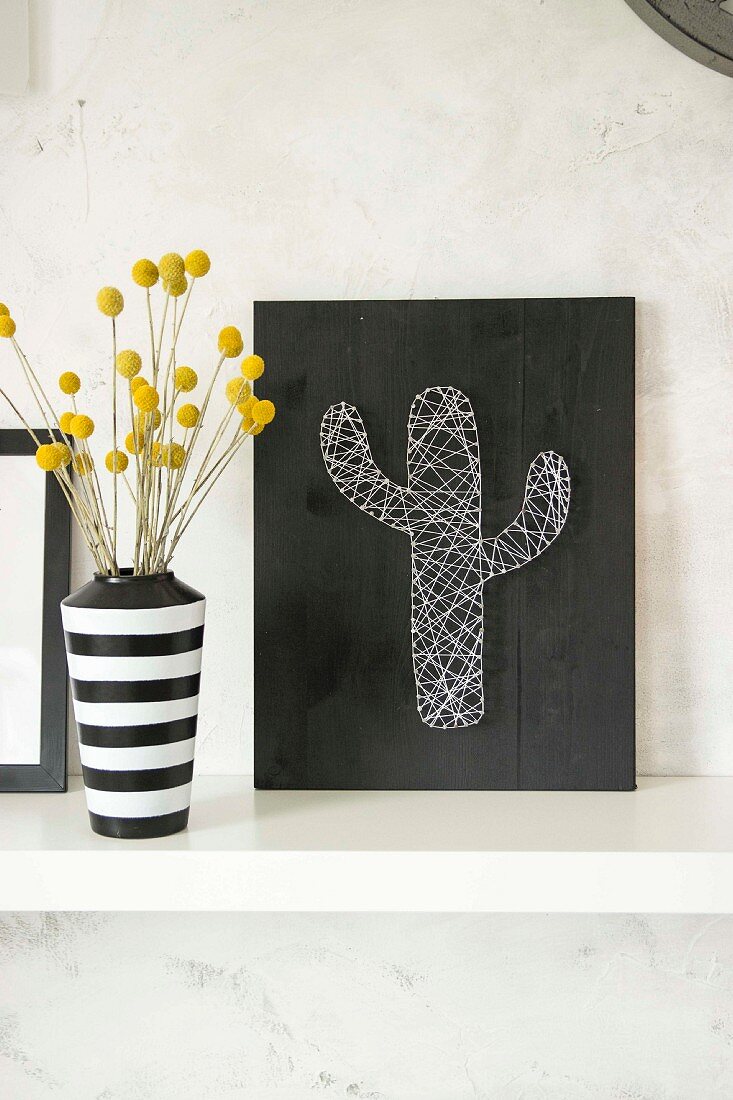 String art picture of cactus and black and white stripes vase of dried flowers
