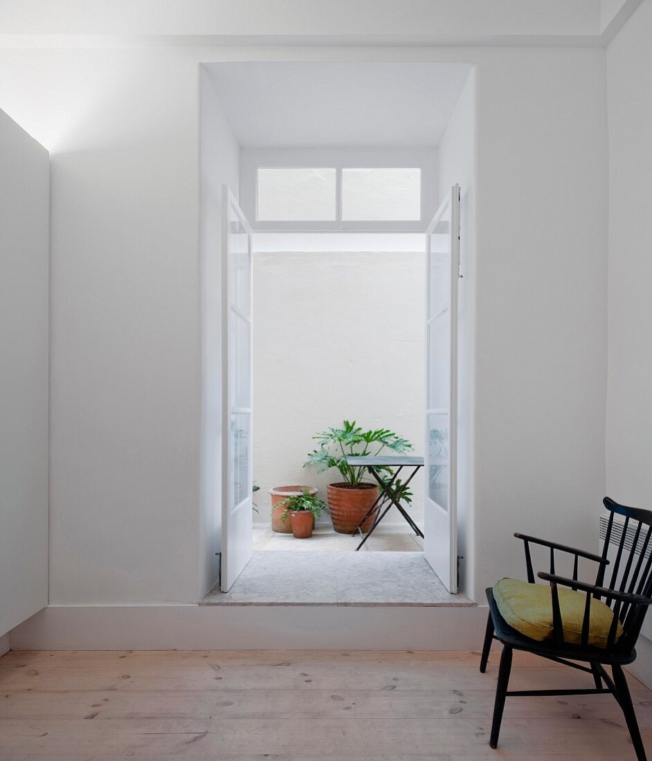 Retro Stuhl mit grünem Kissen in minimalistischem Raum, vor offener Terrassentür und Blick in Innenhof