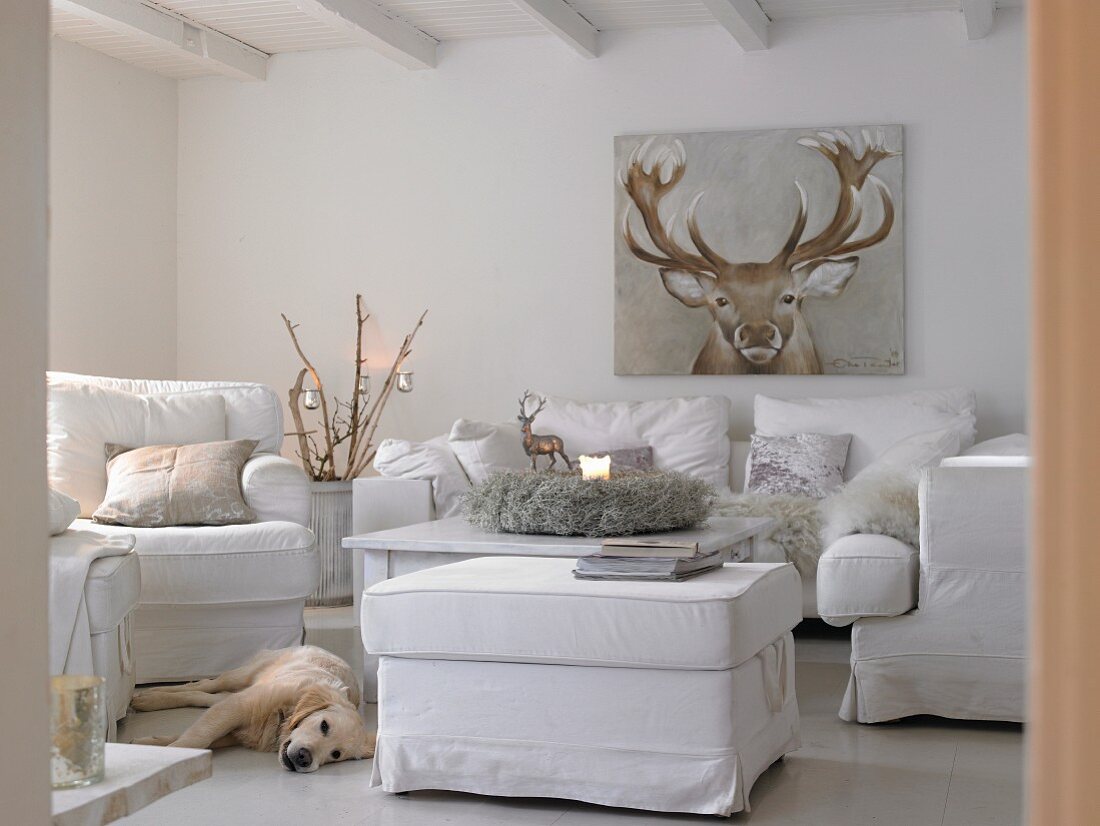 Winterliches Wohnzimmer mit weißen Polstermöbeln, einem Rentier-Bild und einem Hund