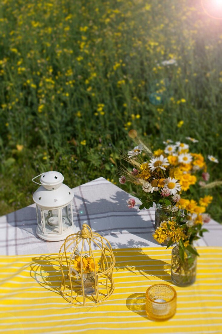 Lantern, ornamental birdcage and posies of wildflowers on yellow and white striped tablecloth outdoors