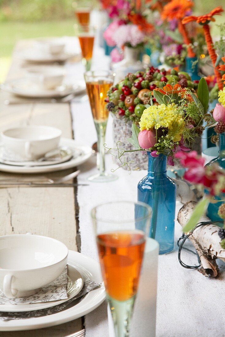 Gedeckter, rustikaler Holztisch mit Aperitifgläsern und Herbstblumen in Vasen