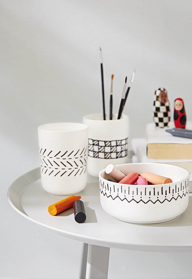 A white bowl and mugs painted with a black pattern