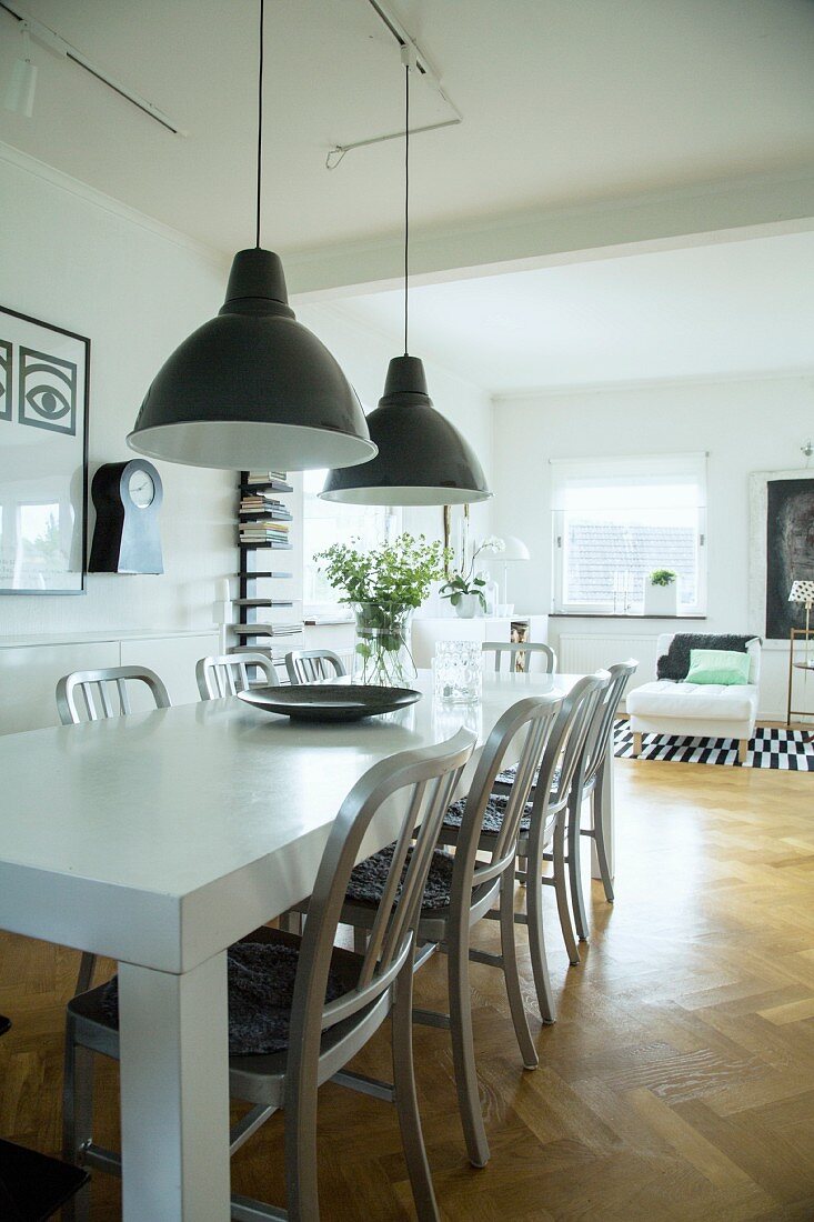 Retro pendant lamps above white-painted table and wooden chairs in open-plan living area
