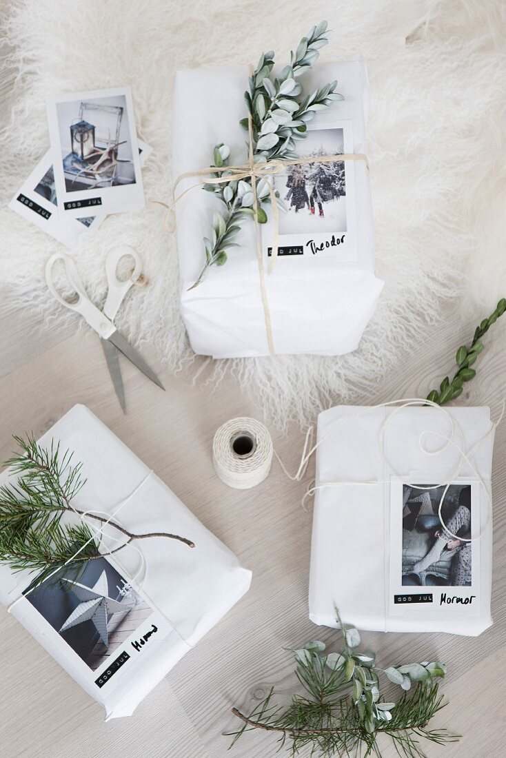 Weiß verpackte Weihnachtsgeschenke mit Zweigen und Fotokarten dekoriert